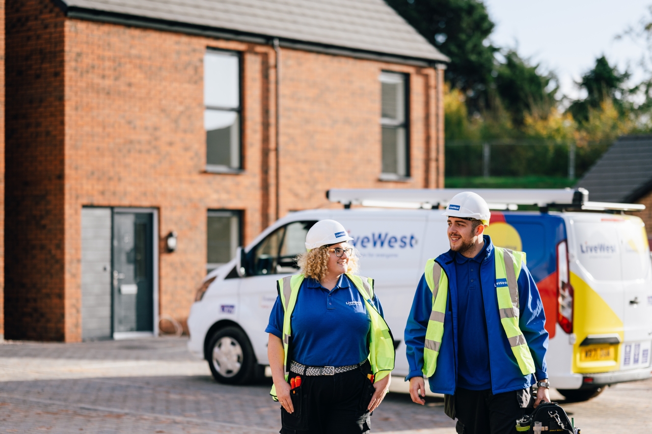 Two LiveWest colleagues wearing safety equipment walking away from their van whilst smiling. 