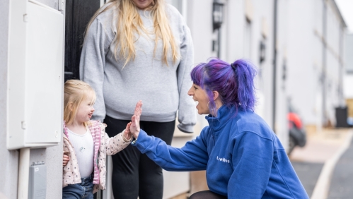 LiveWest colleague high fiving a child outside a house, with the mother standing next to the child. 