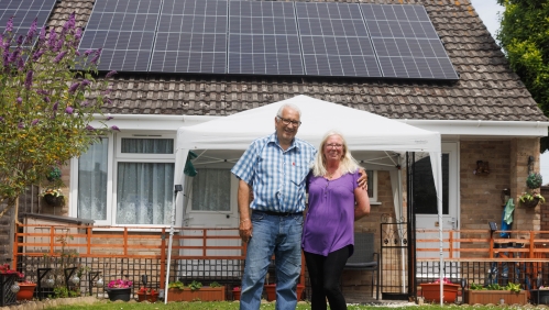 Malcolm and Michelle stood outside their home with solar panels on the roof.